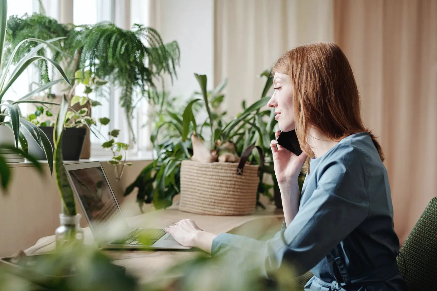 Moça falando ao telefone diante do notebook, em casa