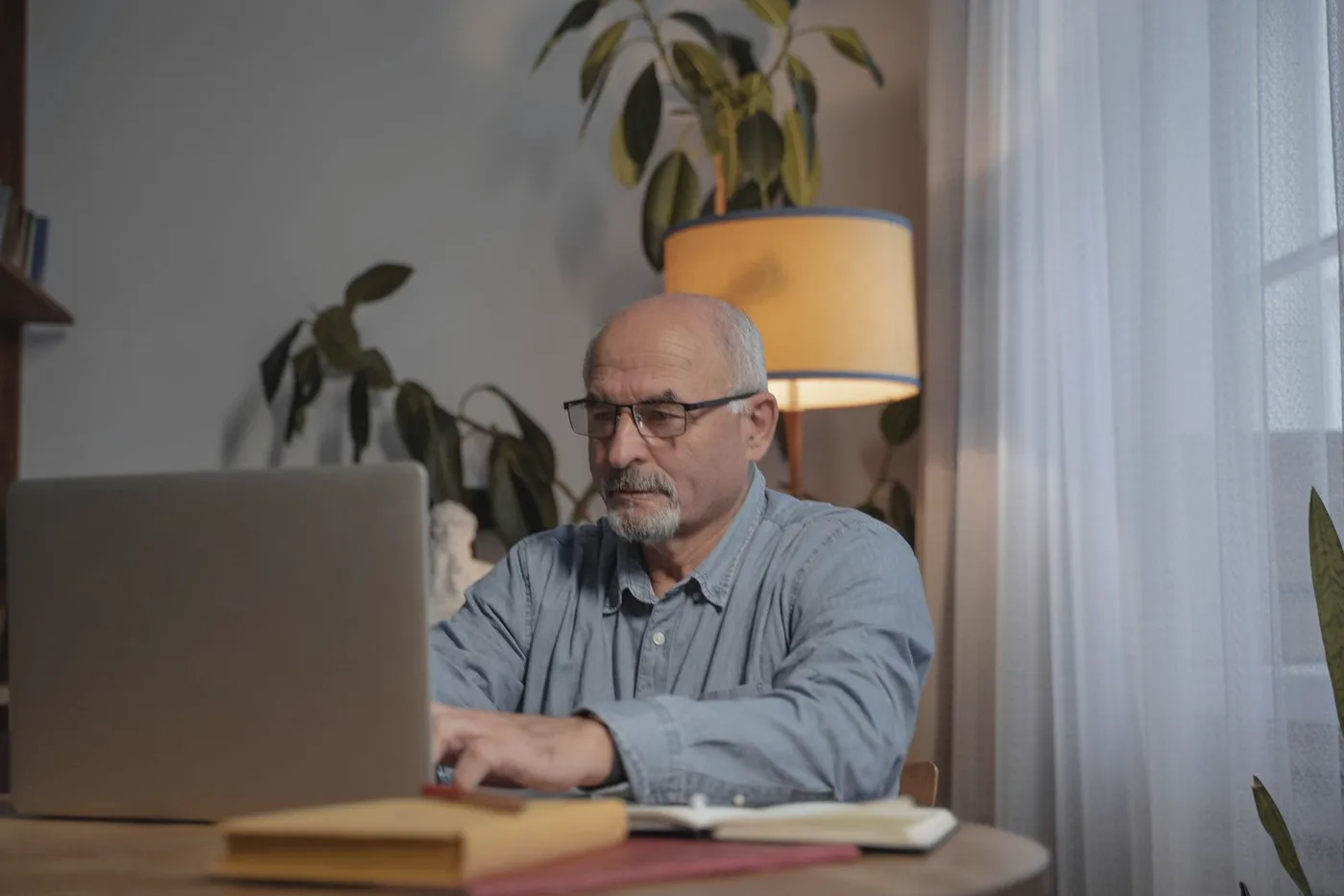 Senhor de óculos respondendo e-mails no notebook em casa