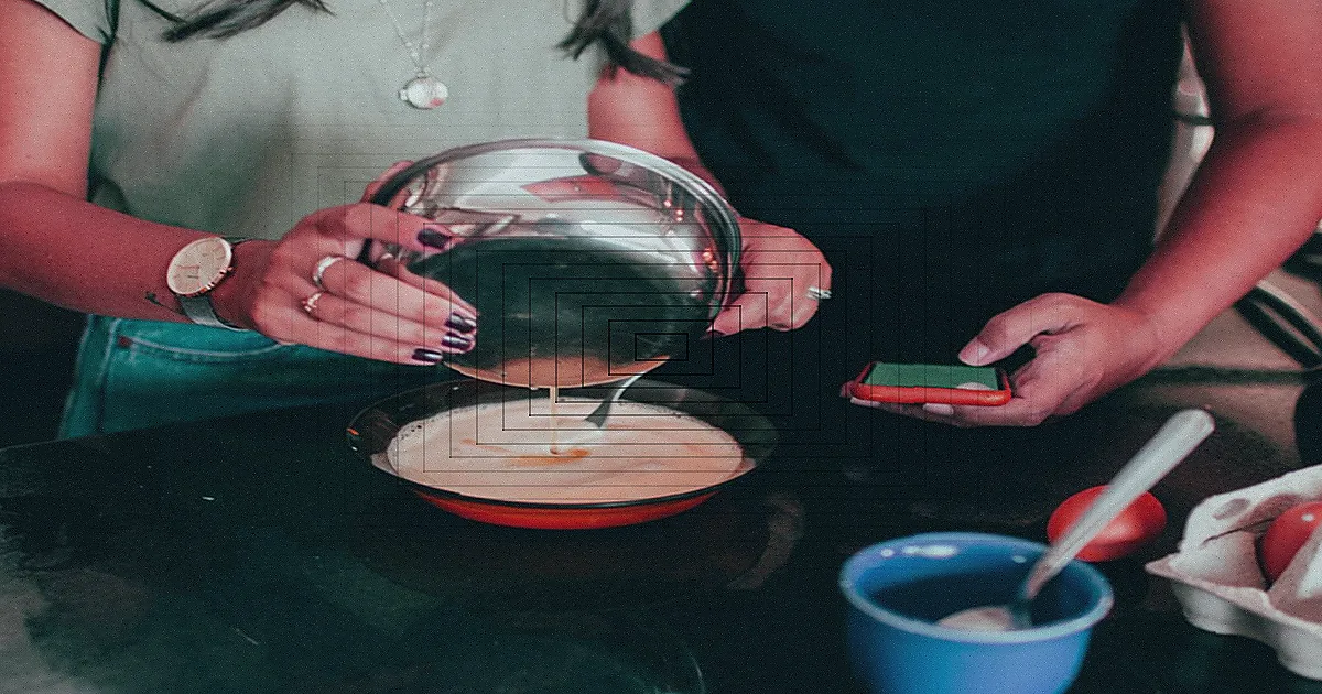 Mãos usando um tablet na cozinha, com vegetais frescos ao lado.