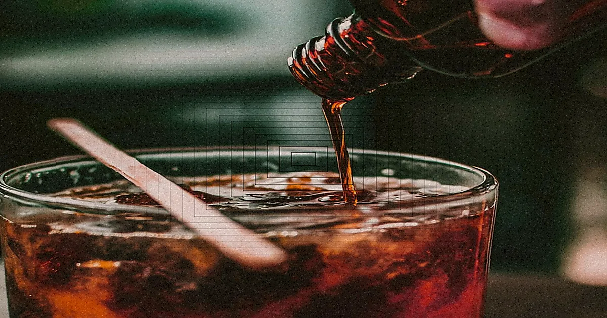 Mãos preparando um coquetel com gelo em um copo de vidro.